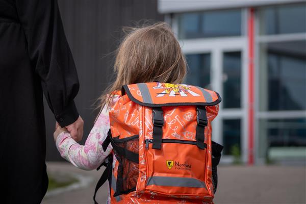 Elev som skal starte på skolen. Orange skolesekk på ryggen og ser mot skolen